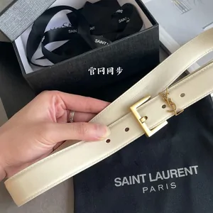 Cream leather belt with a gold buckle, held above its box and dust bag