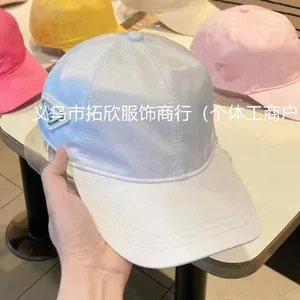 A hand holding a pale silver baseball cap, with pink and yellow caps behind it