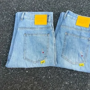 Two pairs of light-wash jeans seen from the back, with yellow patches at the waistband