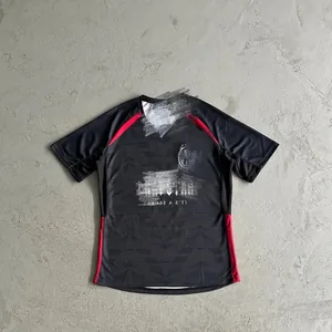 Black short-sleeve sports shirt with red side panels, laid on a gray floor
