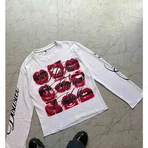 White long-sleeve tee with a block of red printed graphics on the chest, laid on a gray floor